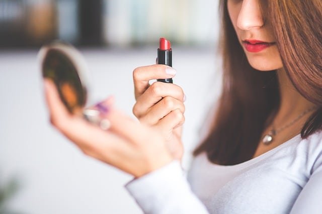 Mulher segurando batom vermelho e espelho de maquiagem com autoestima elevada