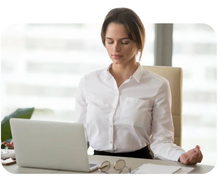 Mulher de camisa branca no escritório praticando mindfulness na frente do notebook